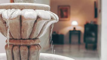 Een marmeren fontein met stromend water, geplaatst in een hal met muurschildering en een plafondlamp.