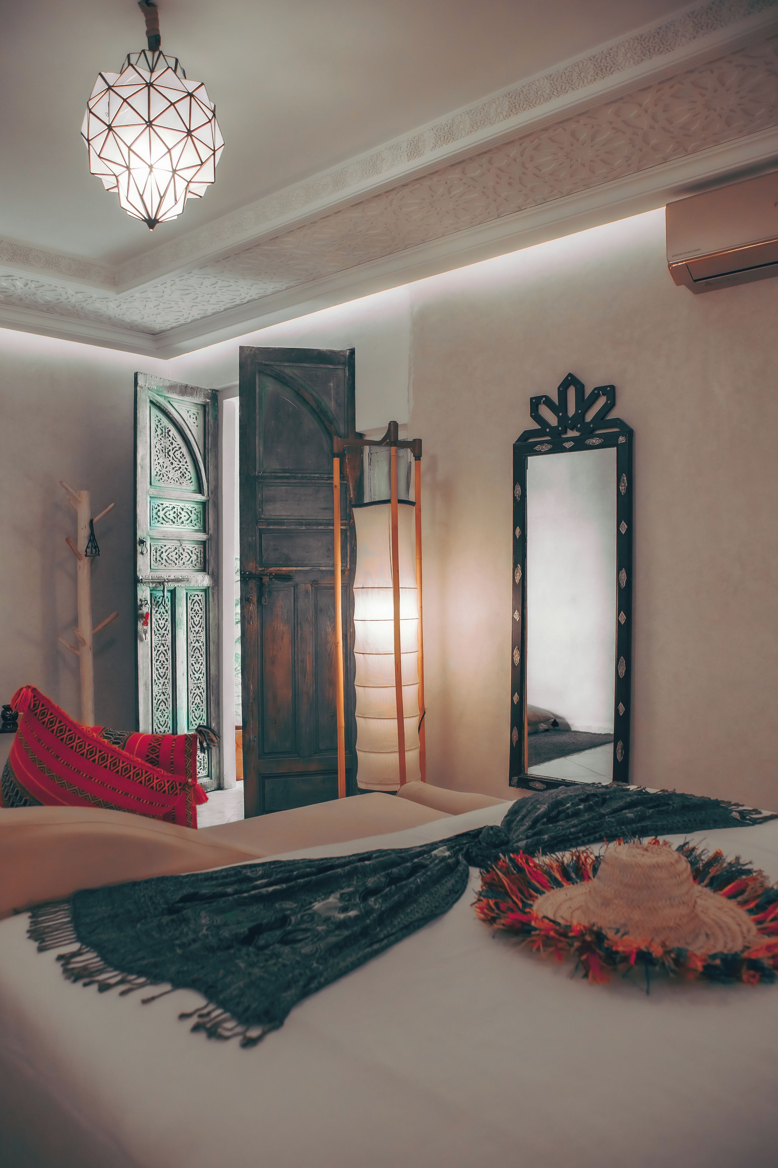 Ein Zimmer mit einem Bett, einer Pendelleuchte, einer Tür mit aufwendigen Verzierungen und einem Spiegel mit dekorativem Rahmen.
