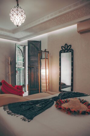 Una habitación con una cama, una lámpara colgante, una puerta con diseños elaborados y un espejo con marco decorativo.