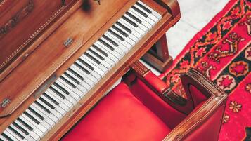 A grand piano with a red bench in a room with patterned carpet.