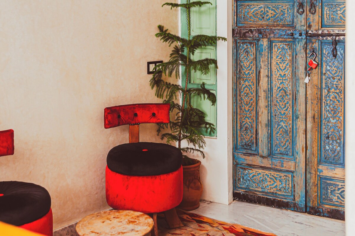 A room with a blue door, a green door, a red chair, a potted plant, and a small stool.