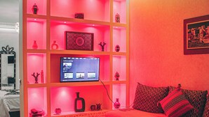 A modern living room with a red-lit shelving unit, a flat-screen TV, and a red sofa. - Riad Tislite & Spa (Marrakech)