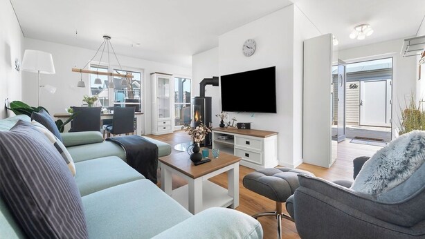 A modern living room with a sofa, a coffee table, and a TV mounted on the wall. - Malte's Ostseekoje- Infrared Sauna, Washing Machine, Terrace, Shower, Fireplace (Olpenitz)