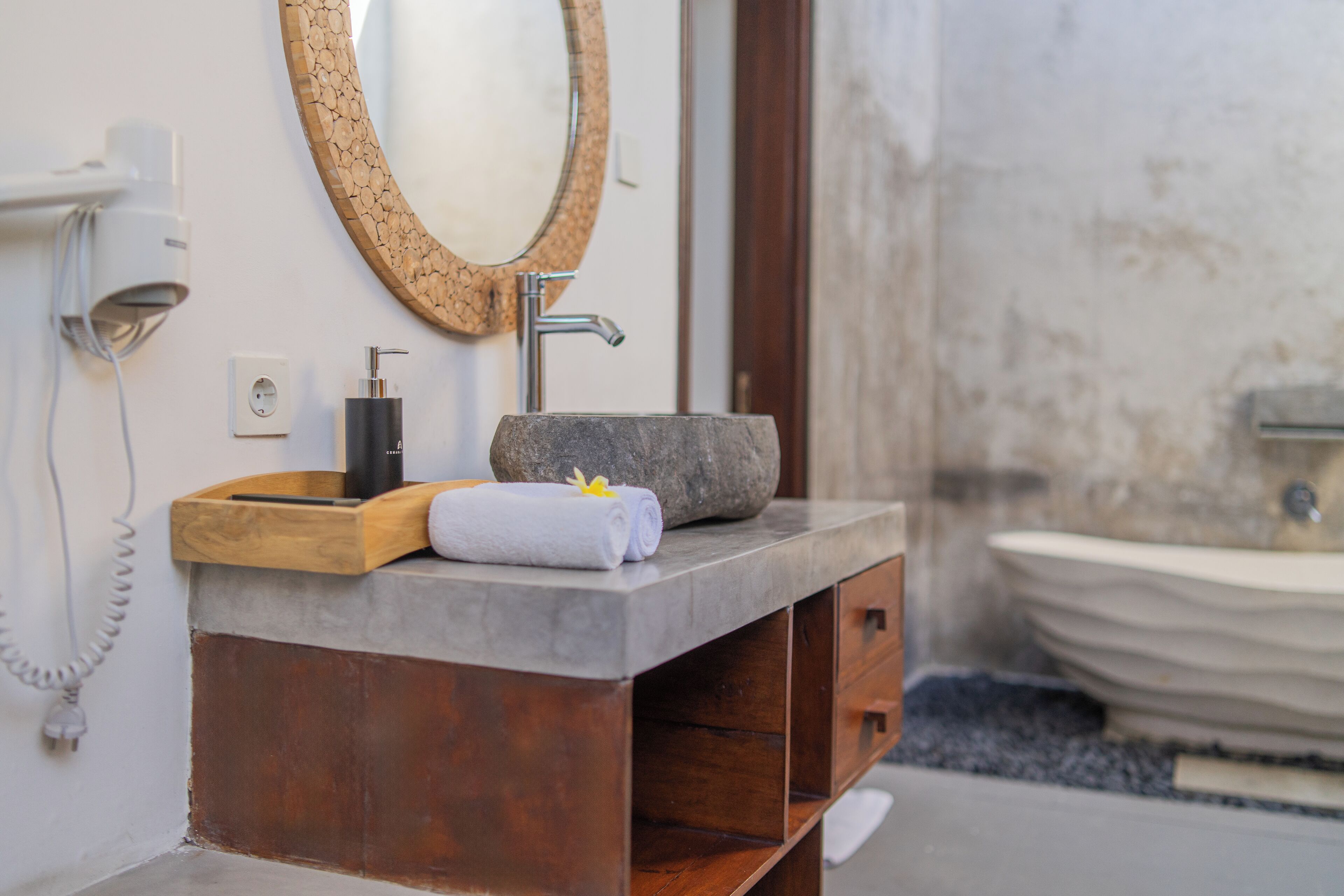 Un bagno con lavabo in pietra, mobile contenitore in legno e specchio con cornice strutturata.