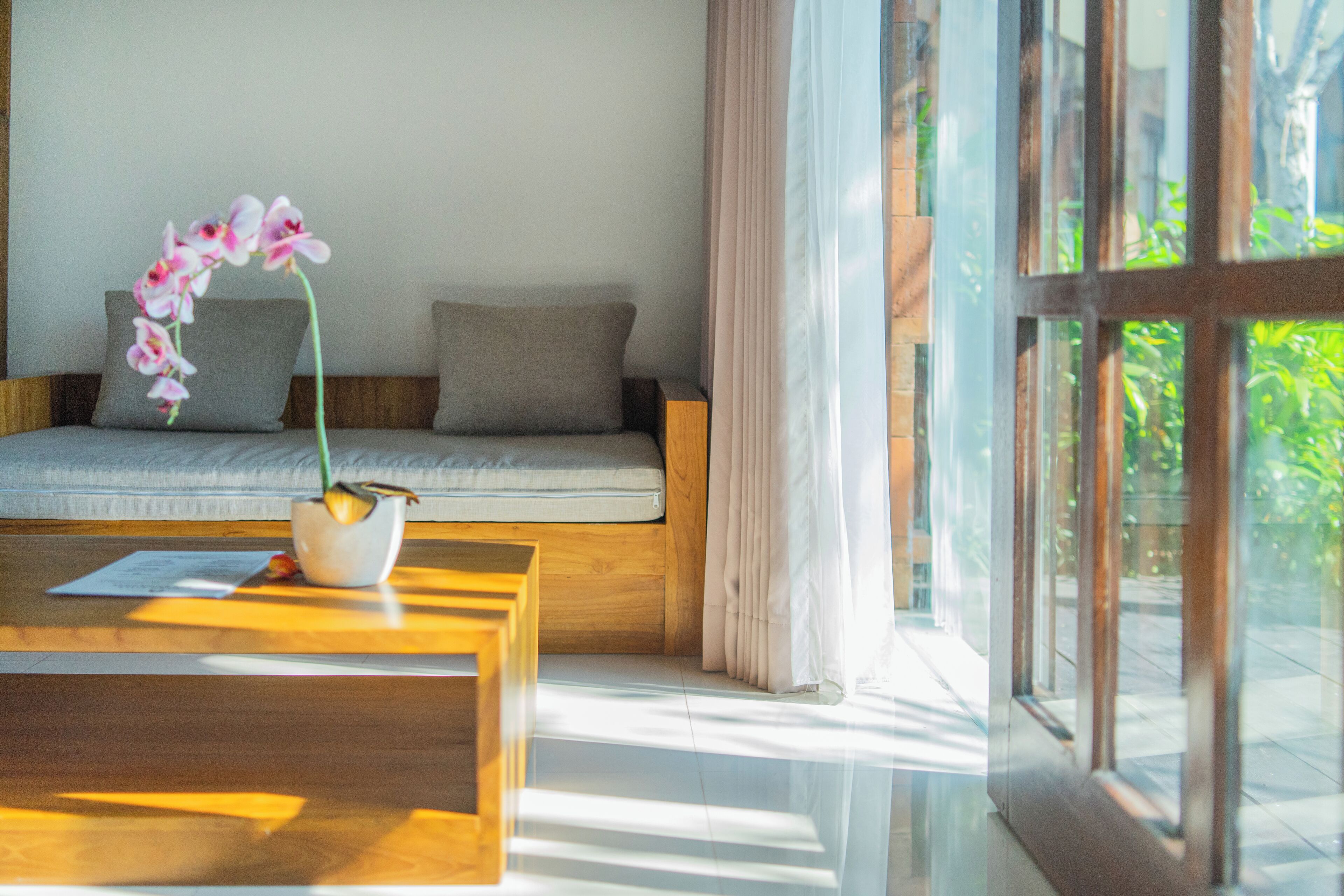 Quarto moderno com mesa de centro de madeira, sofá com almofadas e uma orquídea em vaso.