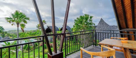 Terraza de madera con mesa y sillas, con vistas a un jardín exuberante y una montaña distante.