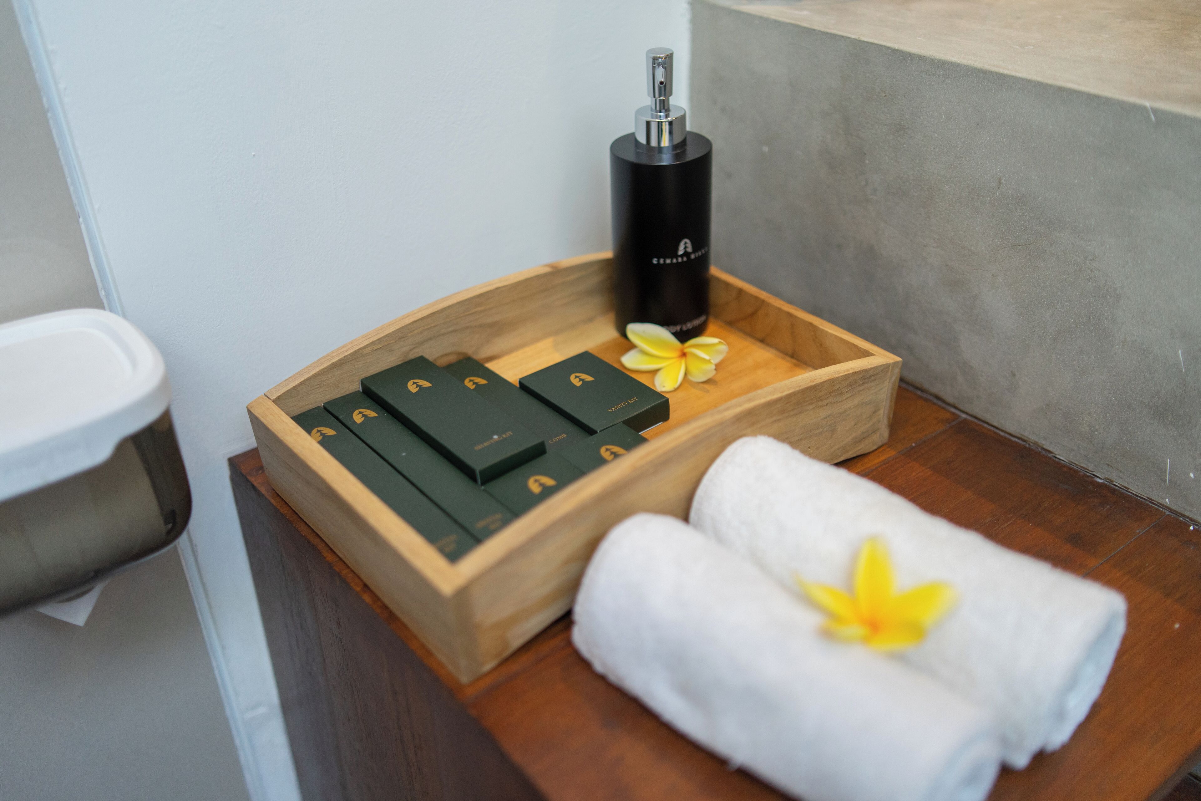 Una bandeja de madera con una botella negra, cajas verdes y toallas blancas con flores amarillas.