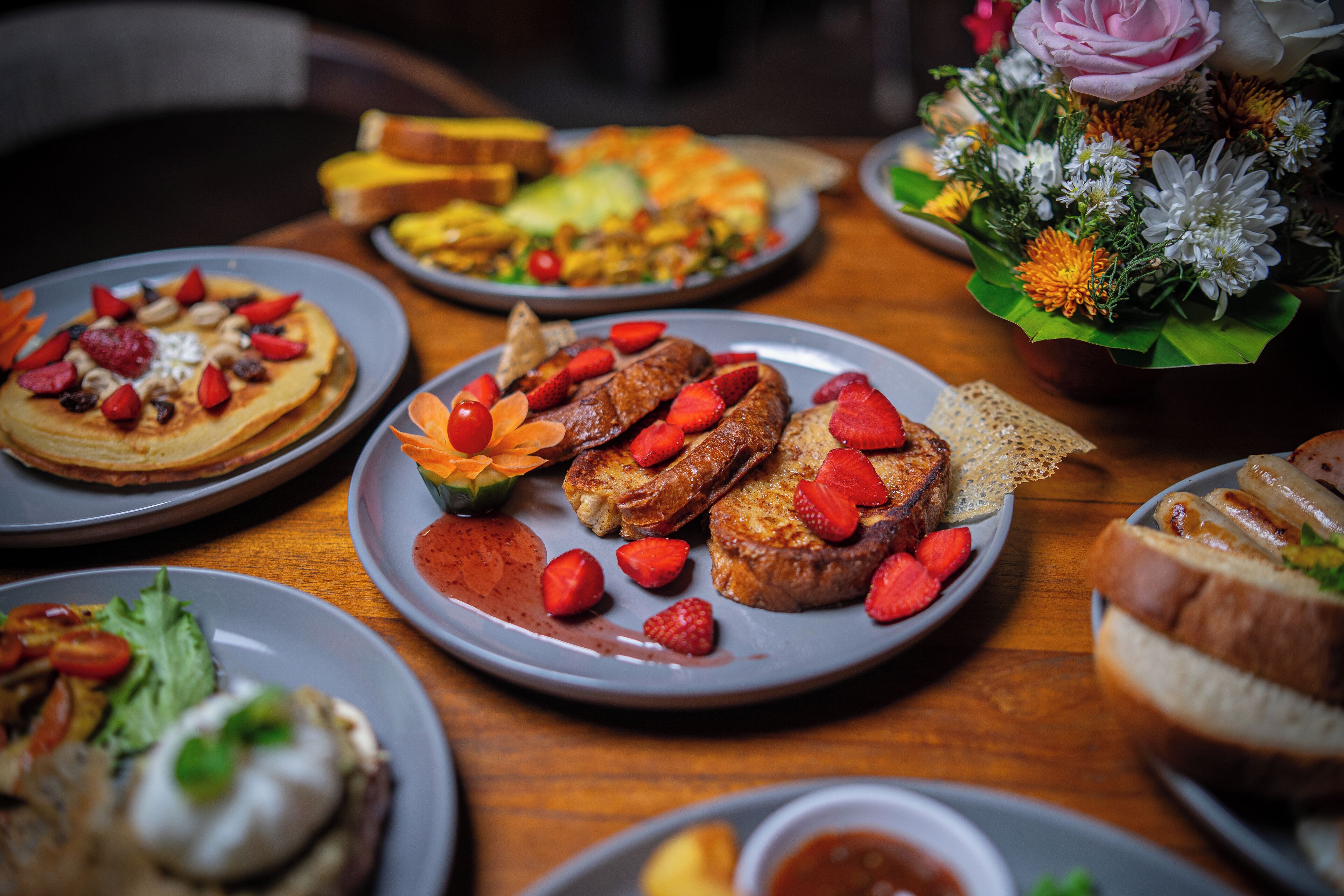 A variety of breakfast dishes on plates, including pancakes, French toast, and toast with strawberries and almonds.