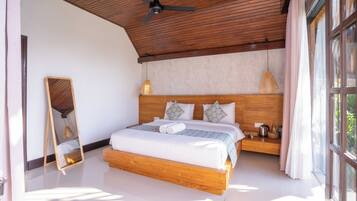 Un dormitorio con estructura de cama de madera, ventilador de techo y un amplio ventanal con cortinas.
