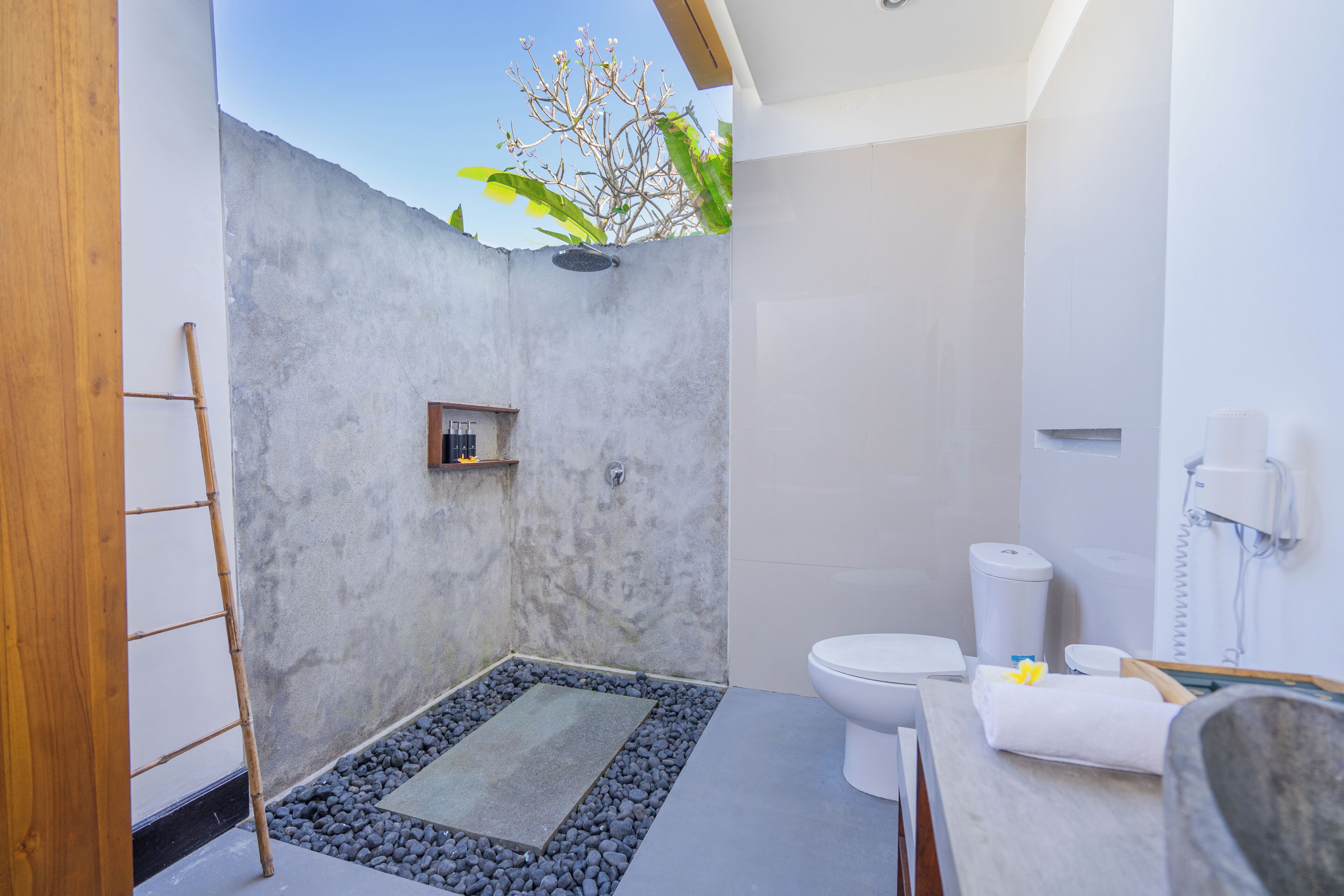 Un baño moderno con zona de ducha de concreto, inodoro y lavabo.
