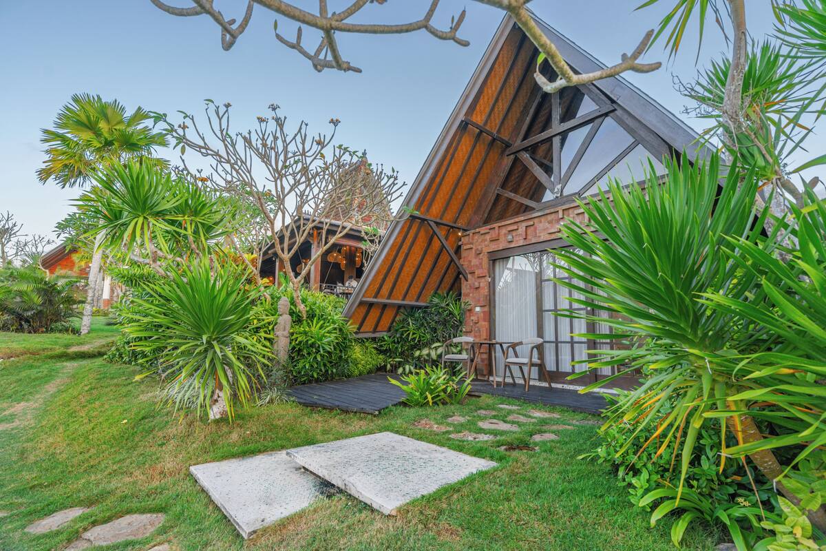 A modern house with a sloped roof, surrounded by a well-maintained garden with various plants and a small patio area.
