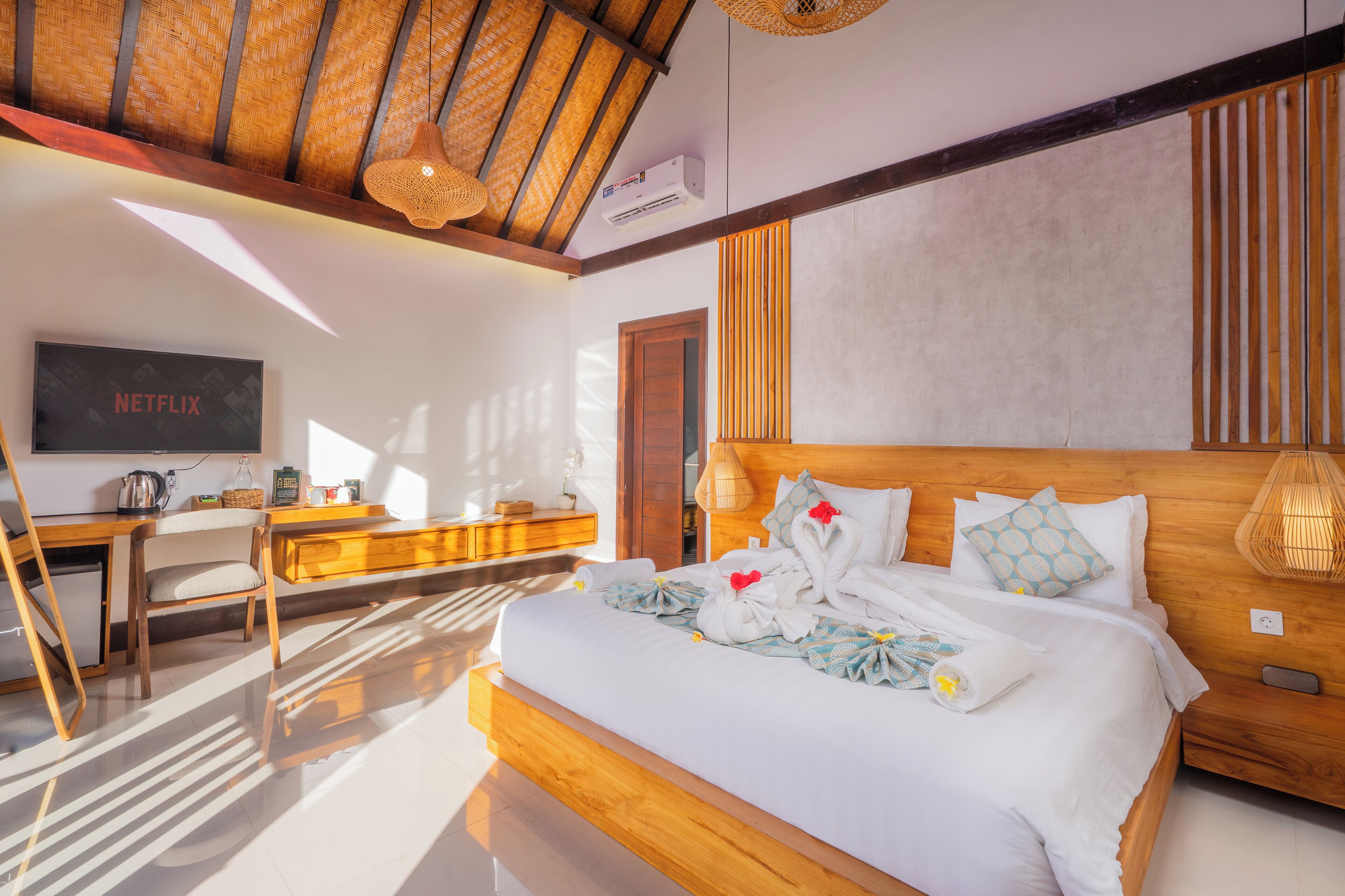 A modern hotel room with a large bed, wooden headboard, and a desk with a chair.