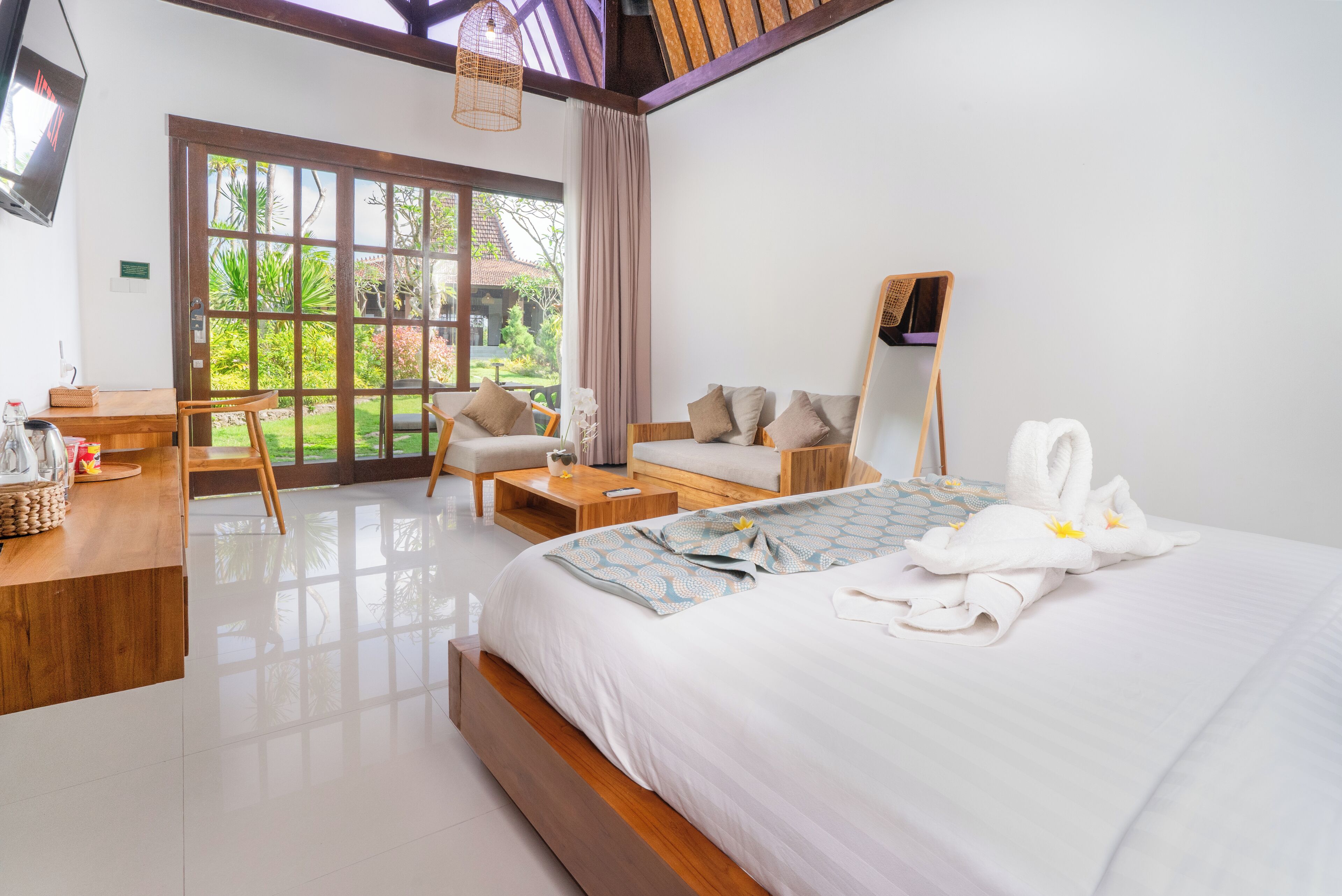 Une chambre d’hôtel moderne dotée d’un grand lit, d’un bureau en bois, d’un canapé et d’une grande fenêtre donnant sur le jardin.