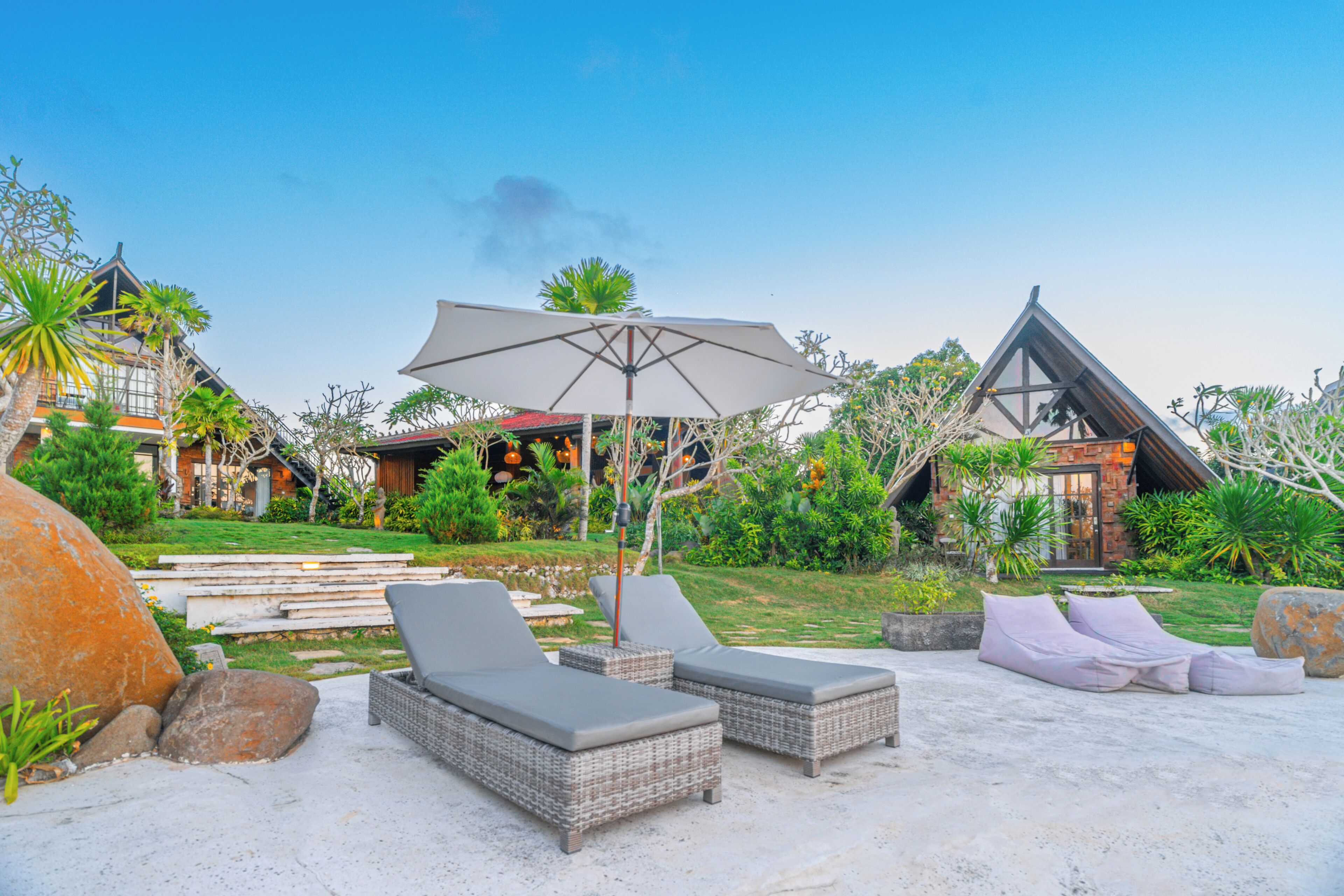 Ein Resort mit Liegestühlen und Sonnenschirm, umgeben von üppiger Vegetation und traditioneller Architektur.