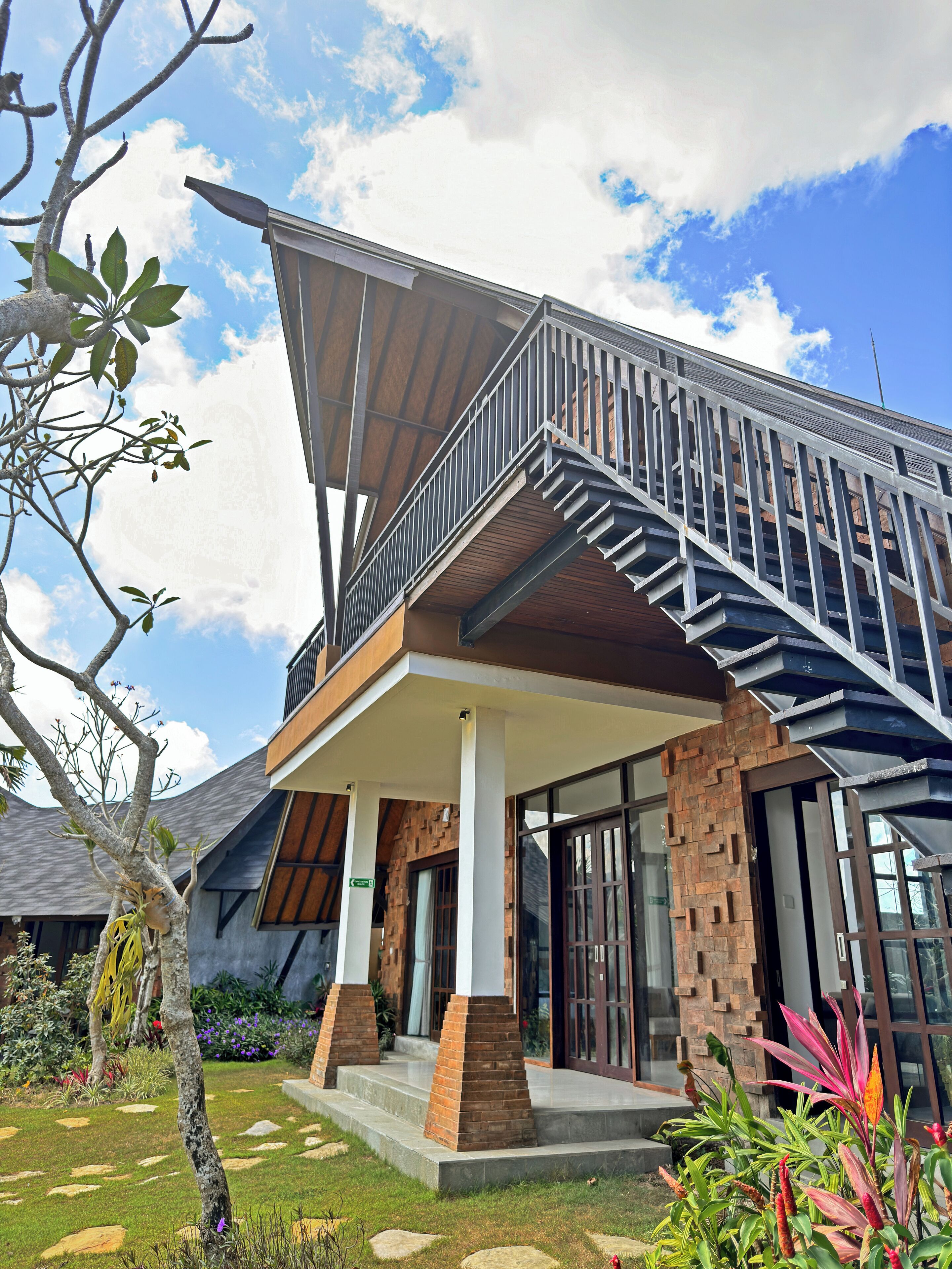 A modern two-story house with a balcony, a stone facade, and a well-maintained garden.