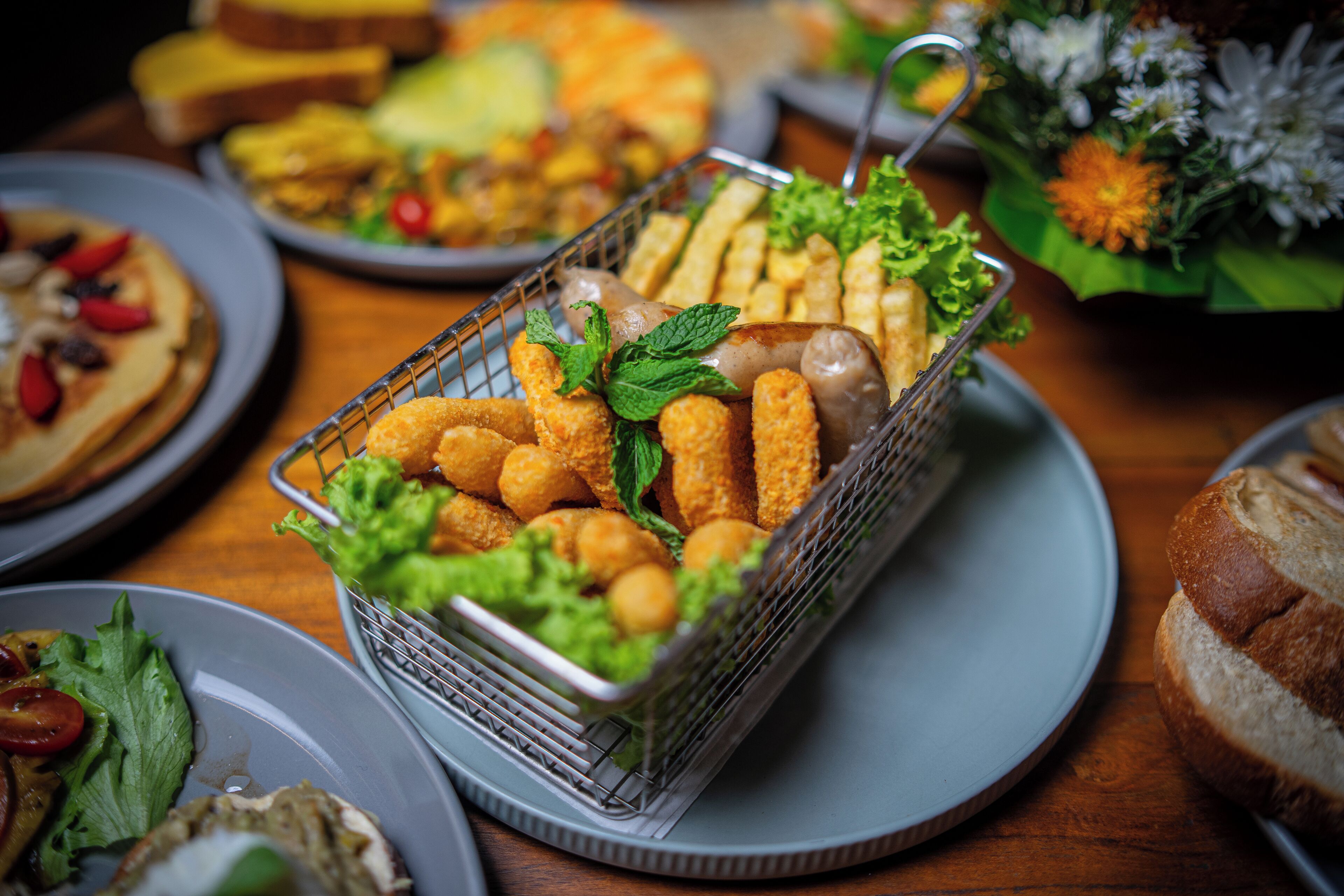 En buffetbord med diverse retter, herunder en kurv med panerede ting, salat og anden mad.