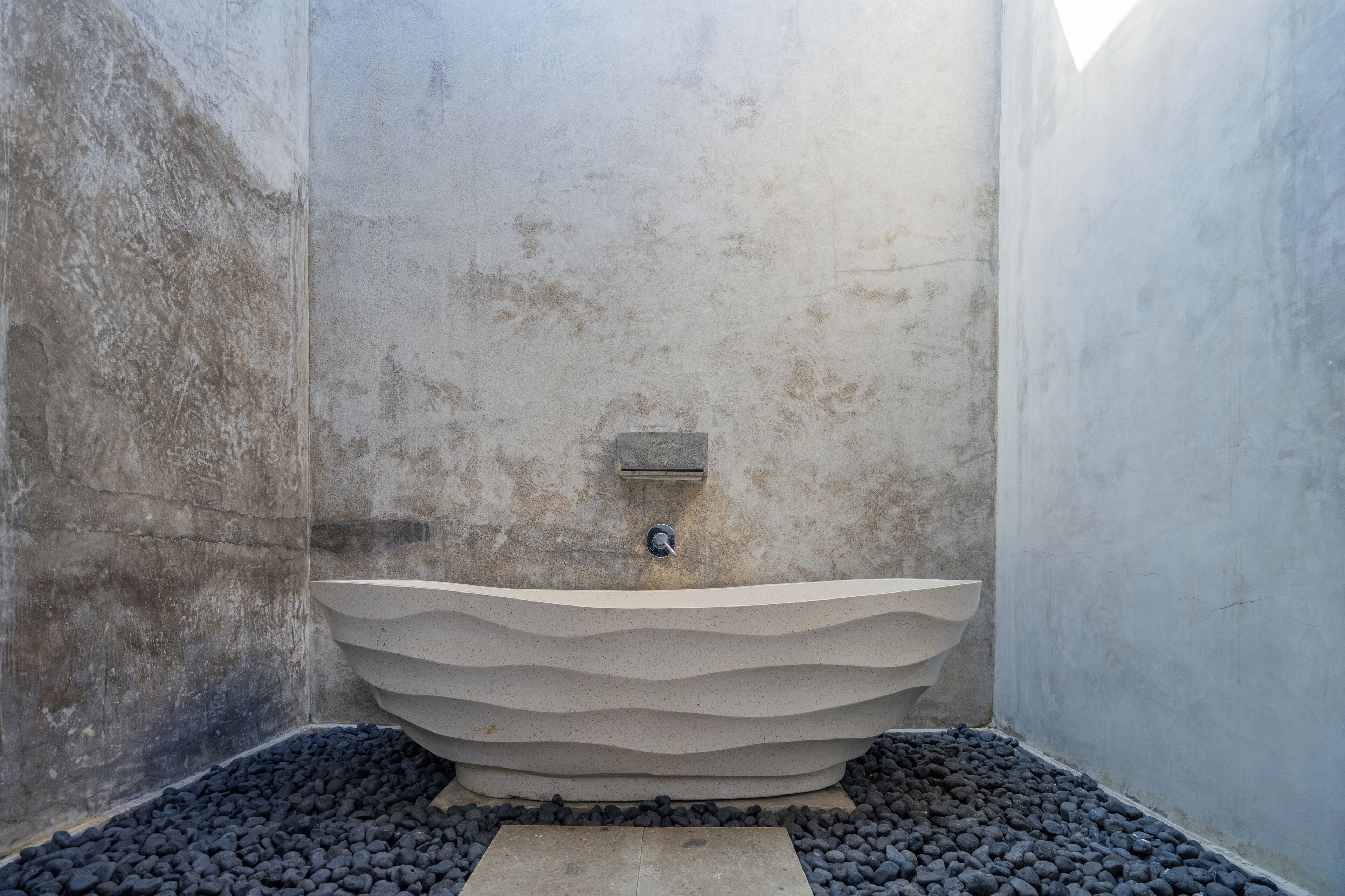 Un baño moderno con un original lavamanos de diseño ondulado, una zona de ducha pequeña y suelo de guijarros.