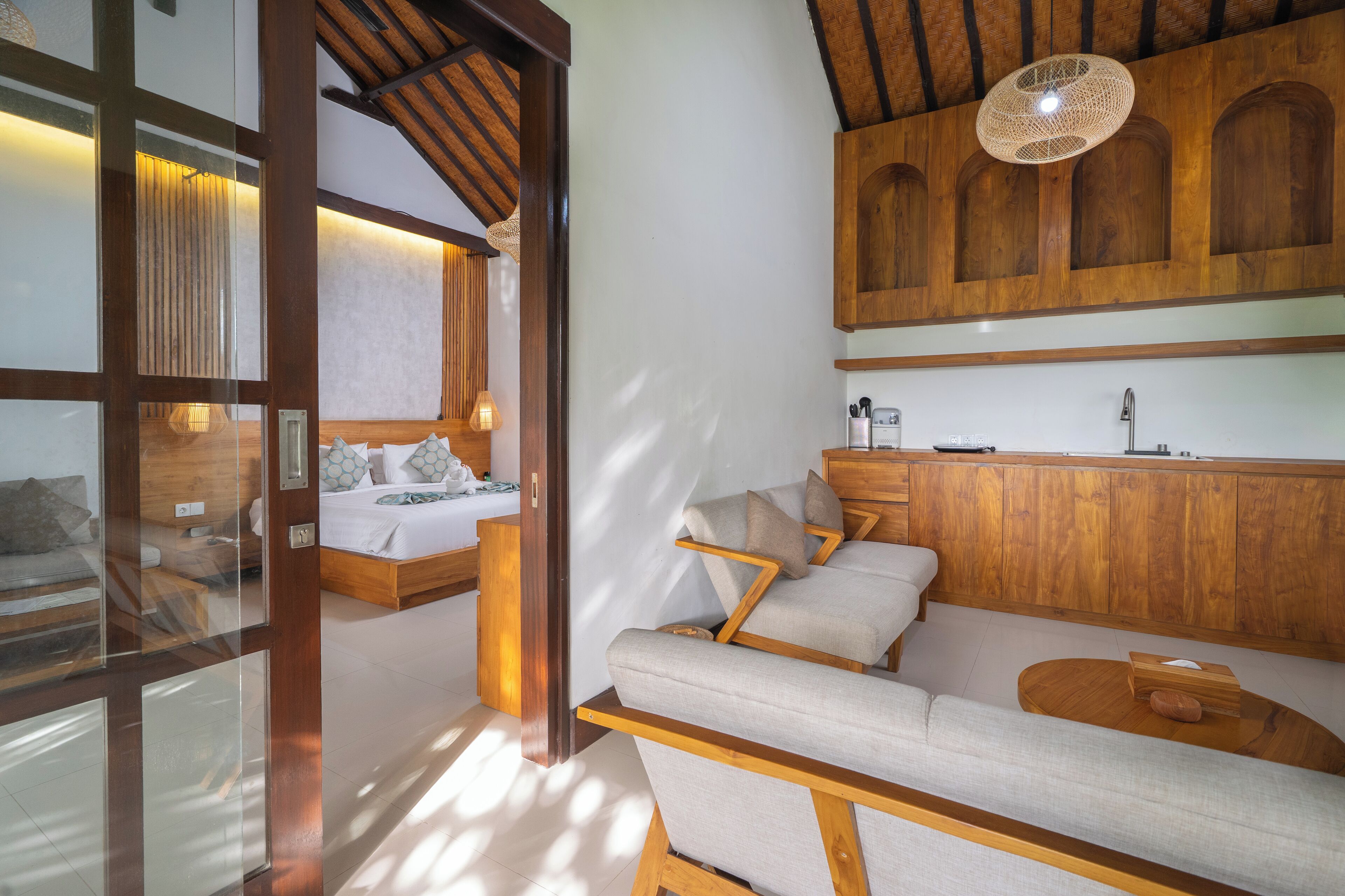 A modern room with a wooden ceiling, a bed with a white headboard, a sofa with cushions, and a wooden cabinet above the sofa.