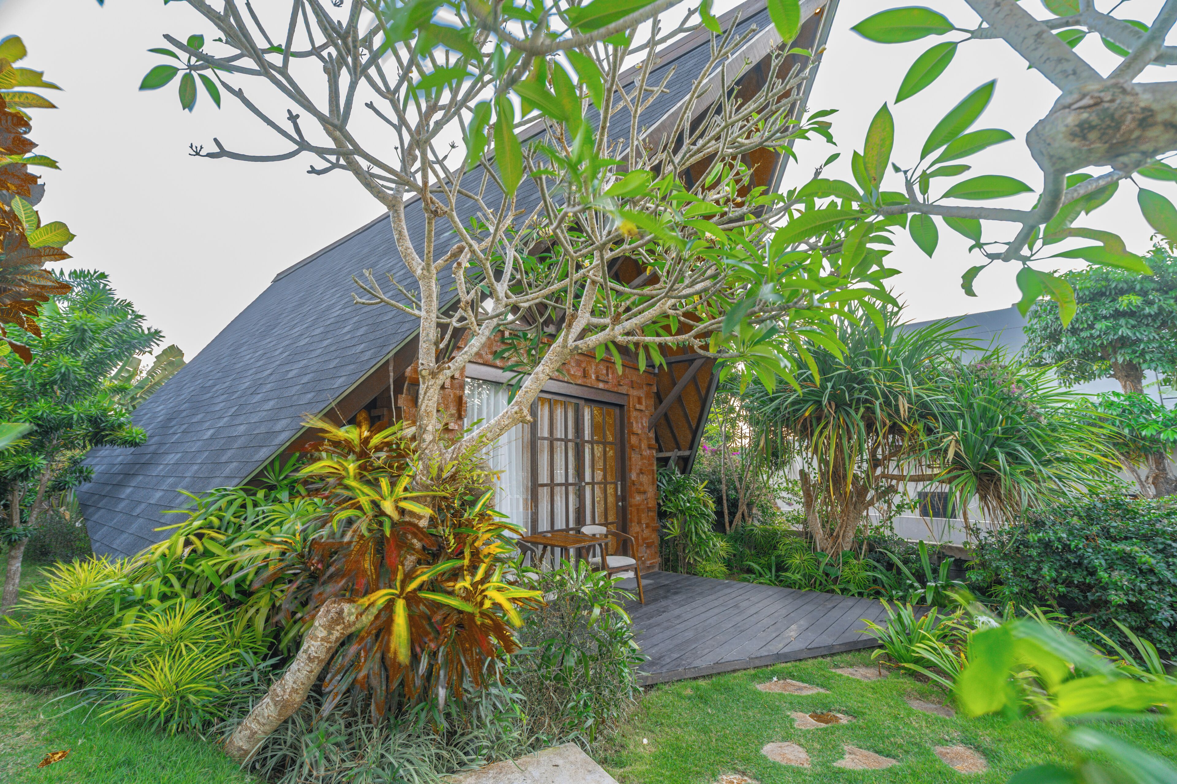 A house with a sloped roof, surrounded by lush greenery and a small patio area.