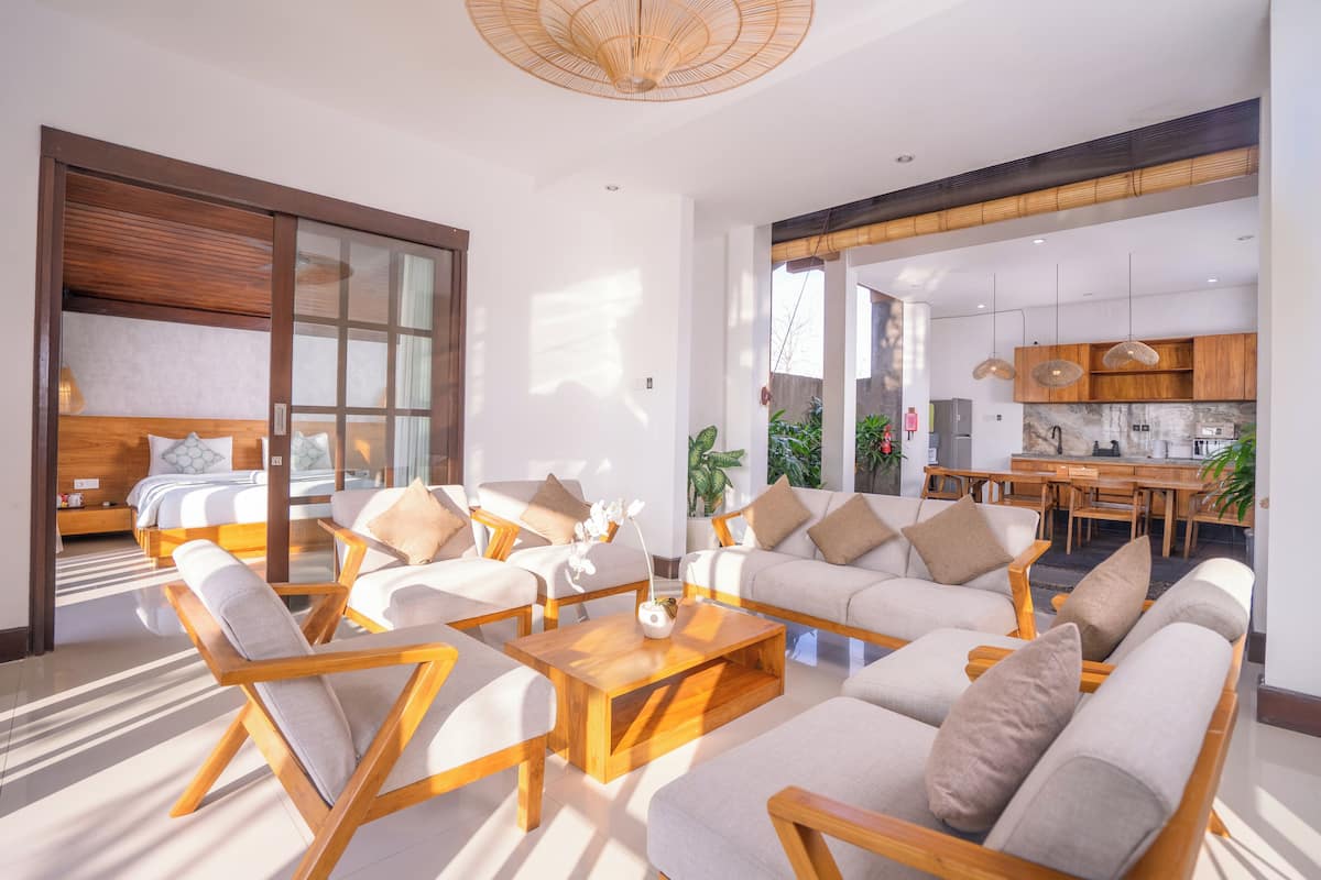 A spacious living area with a sofa set, wooden coffee table, and a large sliding glass door leading to a bedroom.