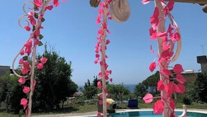 Un área junto a la piscina con una pérgola decorada con flores rosadas y una maceta colgante.