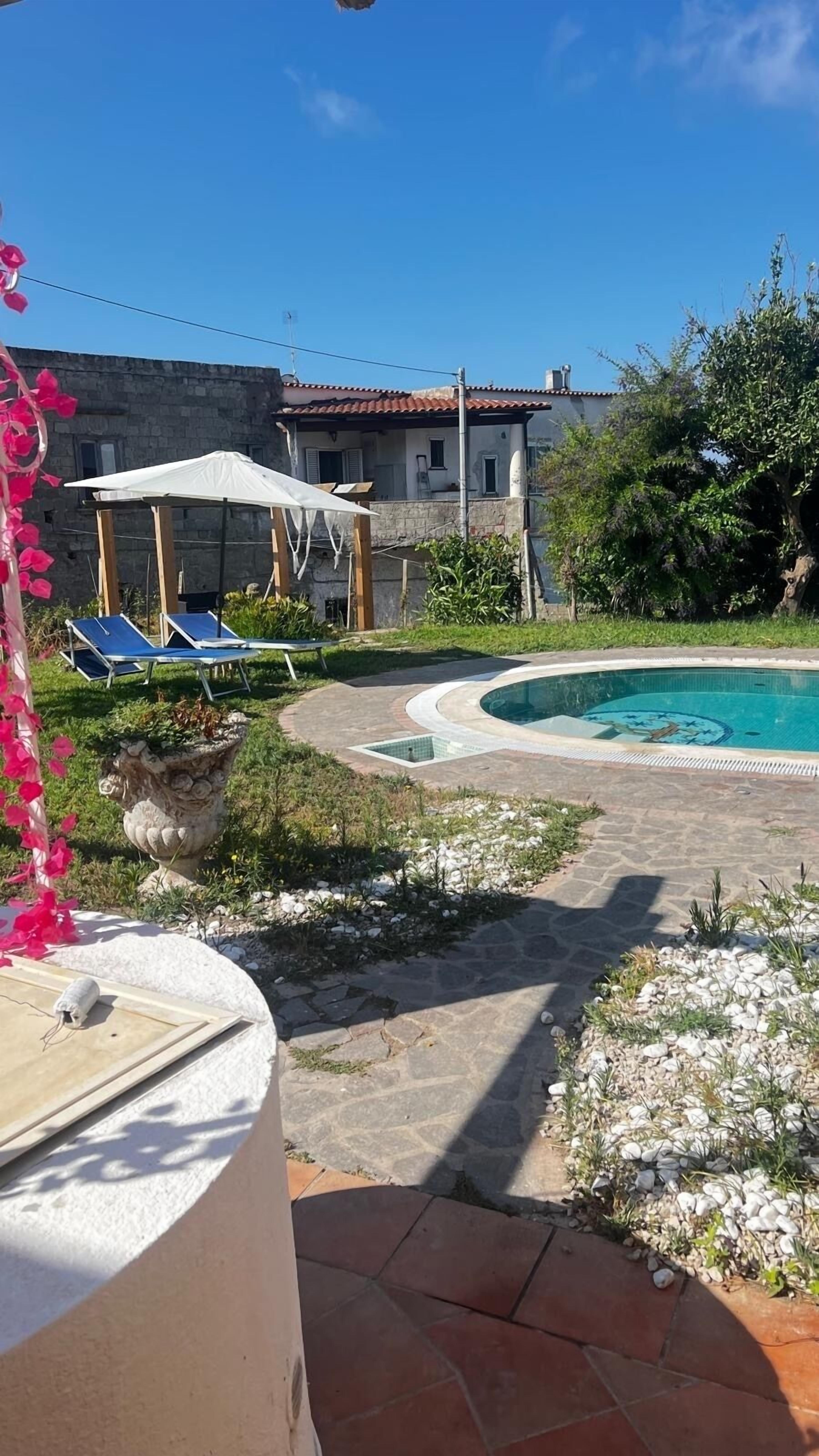 Ein Poolbereich mit einem Kiesweg, einer Pergola mit weißem Baldachin und einem Steinhaus im Hintergrund.