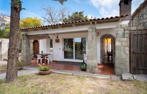 A stone building with a covered patio, a wooden door, and a small table with chairs.