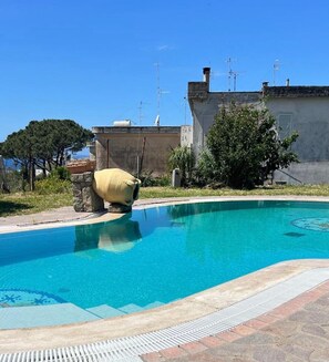 Une piscine dotée d’une structure en pierre, un ciel d’un bleu limpide et des bâtiments en arrière-plan.