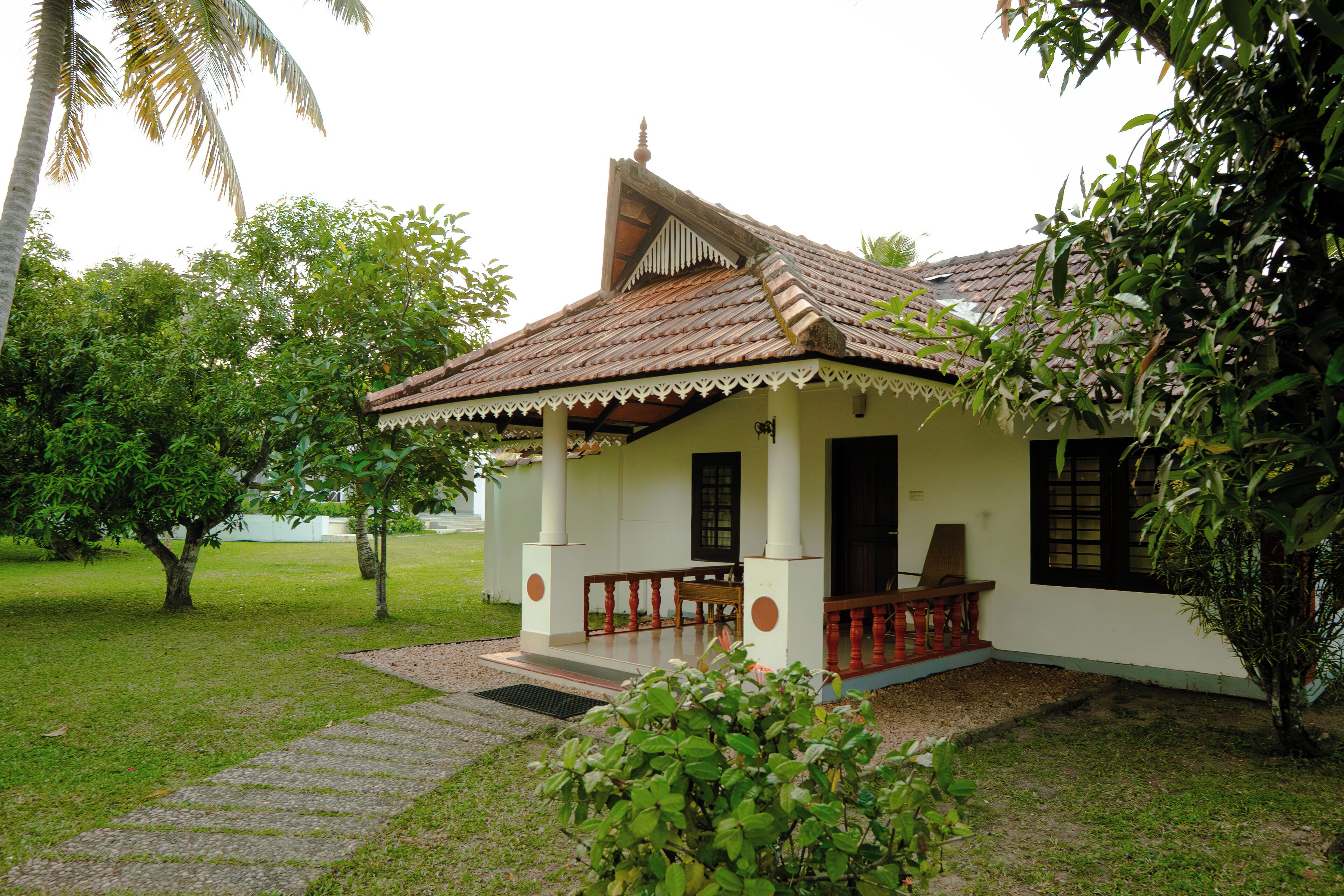 A single-story building with a tiled roof, a porch with a wooden railing, and a small garden area with a pathway leading to the entrance.