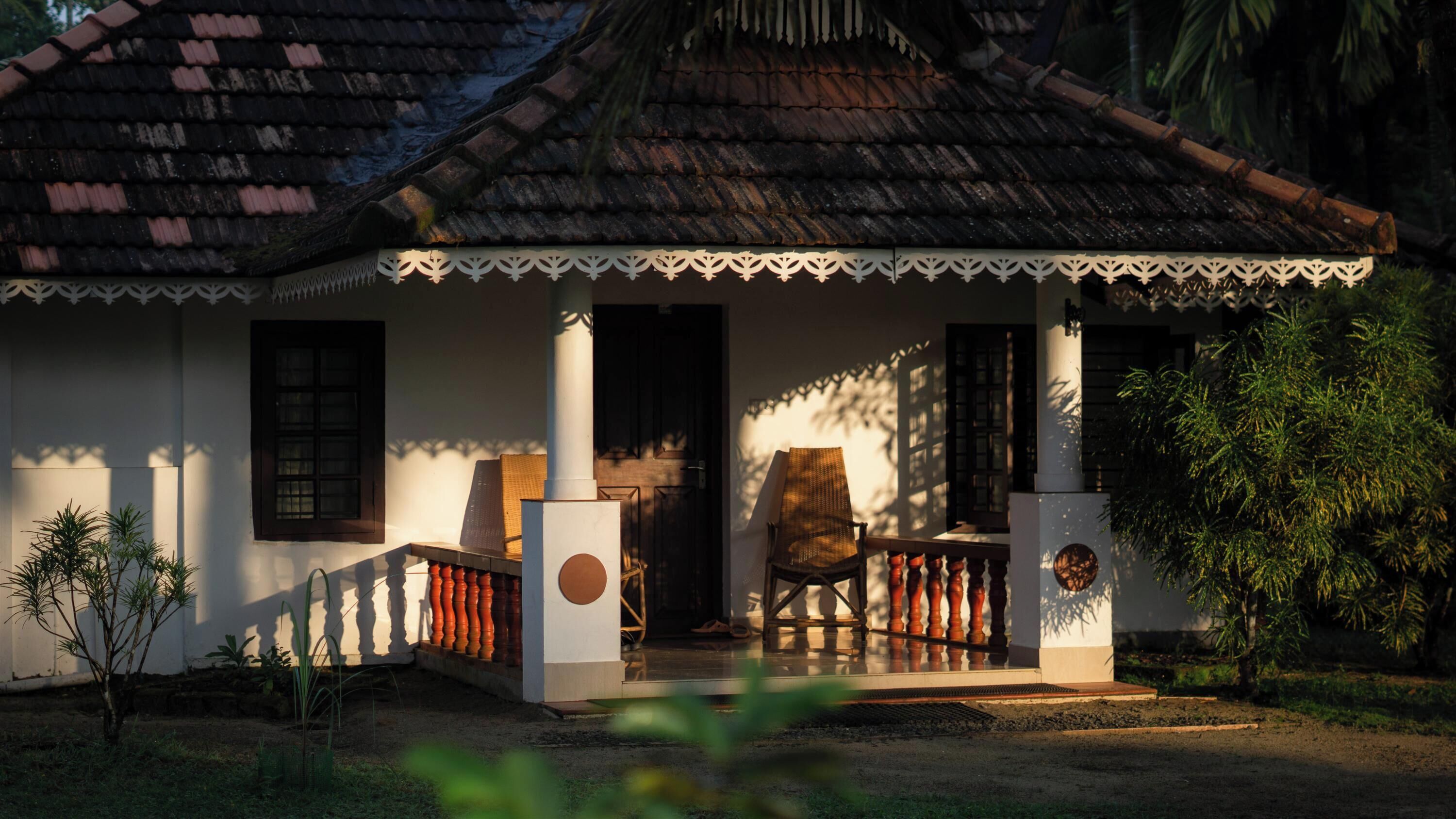 Ein traditionelles Haus mit Ziegeldach, einer Veranda mit Geländer und einem Stuhl davor.