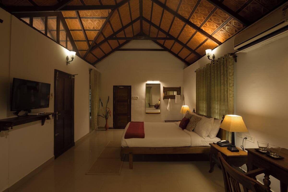 Une chambre d’hôtel avec un plafond haut, un lit, une télévision, un bureau et une lampe.