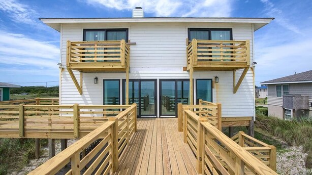A beachfront property with a wooden deck, a white building with two balconies, and a glass door entrance. - The Black Pearl - Oceanfront - North Topsail (North Topsail Beach)