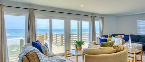 Un salón amplio con un gran ventanal con vistas a la playa, amueblado con un sofá, sillones y una mesa de centro.