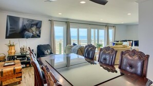 A spacious dining area with a large glass table, leather chairs, and a ceiling fan. - The Black Pearl - Oceanfront - North Topsail (North Topsail Beach)