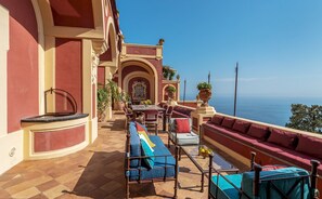 A sunlit outdoor seating area with a terrace overlooking the sea, featuring a table and chairs, a sofa, and potted plants. - Palazzo San Pietro by Elite Villas (Positano)