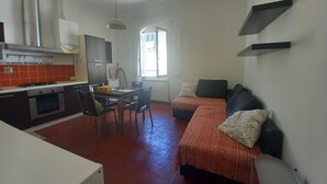 Un espacio habitable compacto con kitchenette, zona de comedor y sofá con cojines.