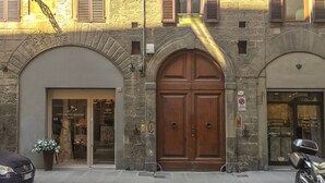 A stone building with a large wooden double door, a shop entrance, and a parked motorcycle. - Maggio 54 in Florence (Florence)