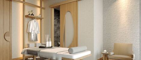 A modern spa room with a massage table, a chair, and a shelf with towels and toiletries.