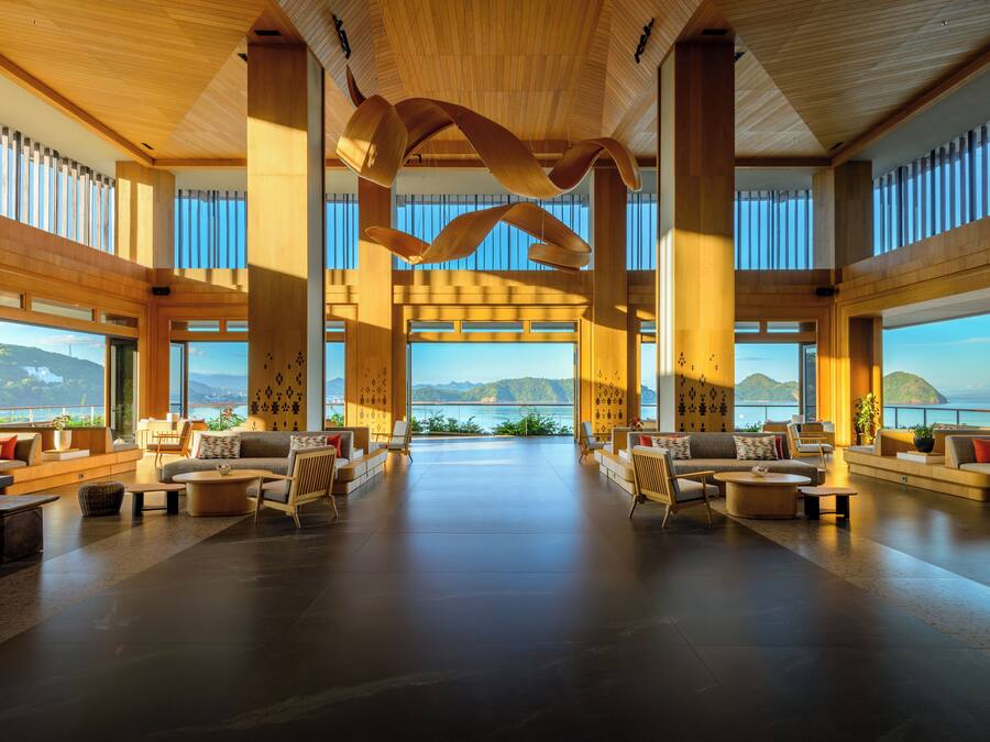A spacious lobby with a view of the sea, wooden ceiling, and modern furniture.