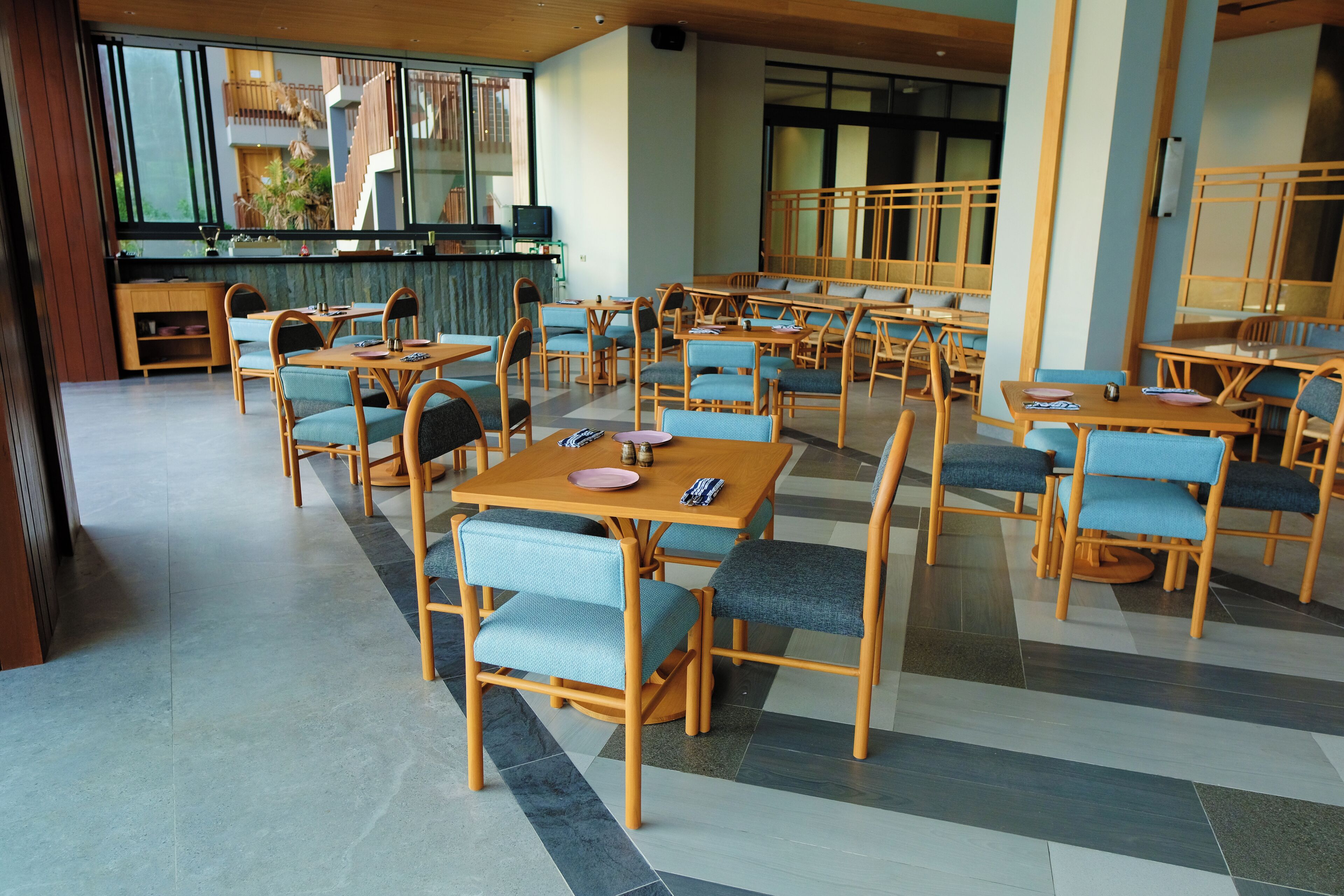 A spacious dining area with multiple tables and chairs, a counter with a television, and large windows offering views of the outside.