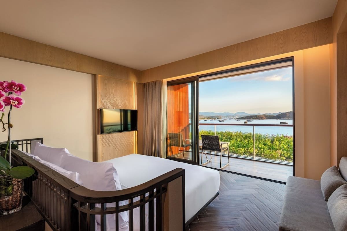 Ein Hotelzimmer mit Bett, Fernseher, Balkon und Meerblick sowie einer Zimmerpflanze.