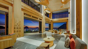 Un hall d’entrée spacieux au design moderne, comprenant un grand espace salon, des éléments décoratifs en bois et de grandes fenêtres offrant une vue sur la mer.