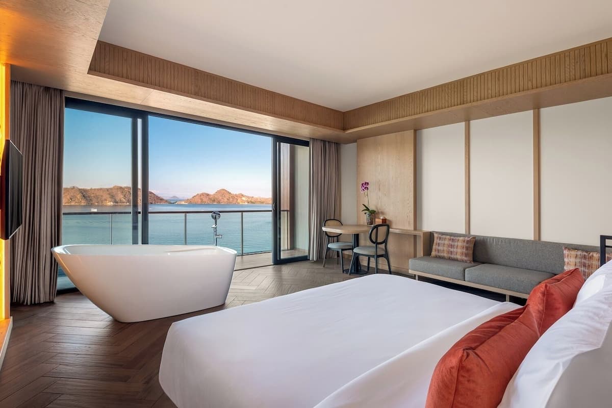 Ein modernes Hotelzimmer mit einem großen Bett, einer Badewanne, einer Sitzecke und einem Essbereich mit Meerblick.