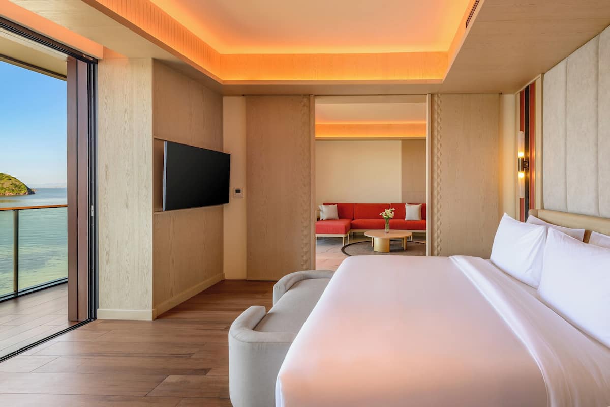 Ein modernes Hotelzimmer mit einem großen Bett, einem Flachbildfernseher, einer Couch und einem Balkon mit Meerblick.