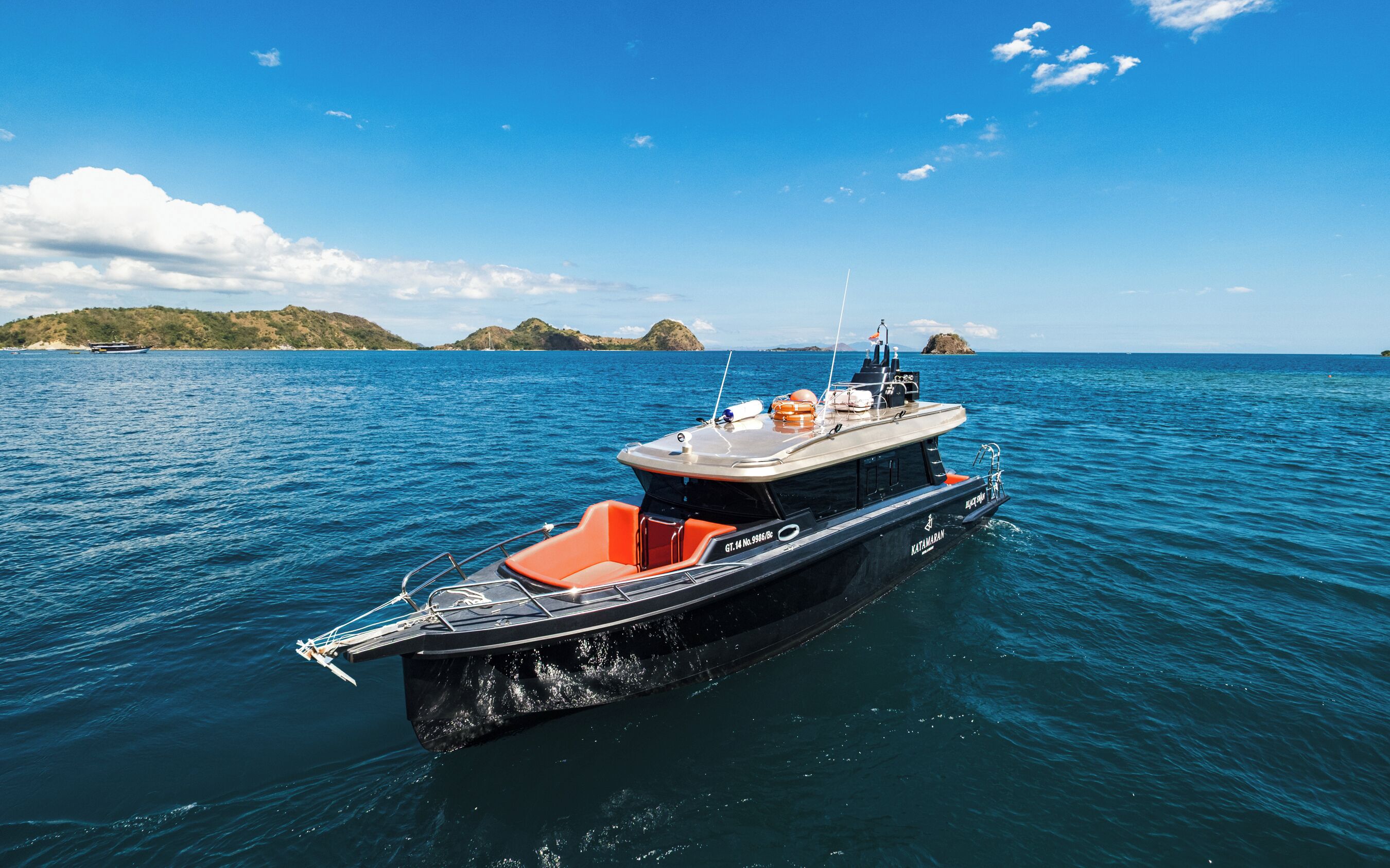 A boat with a cabin and deck seating, sailing on a calm sea with distant islands.