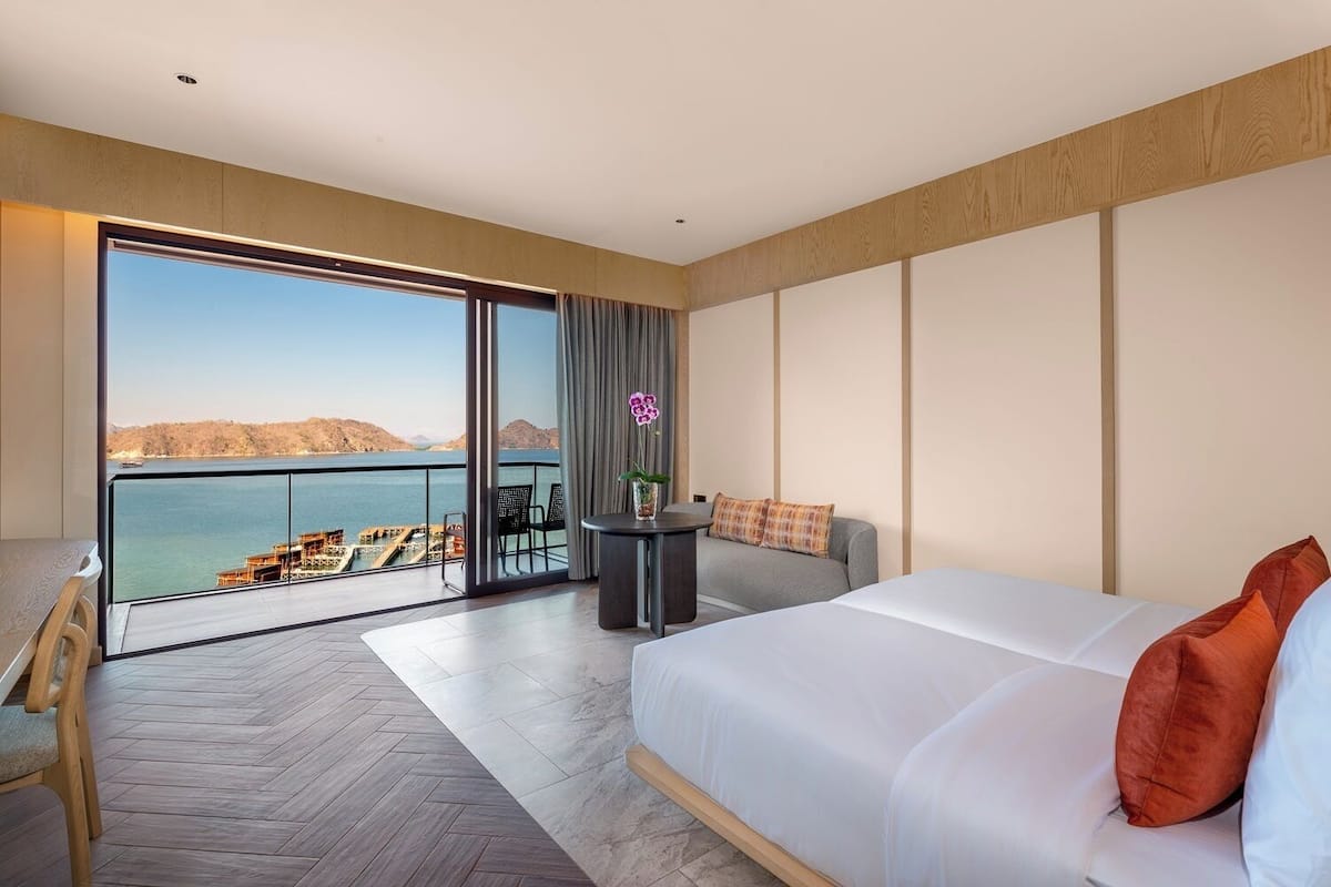 Ein Hotelzimmer mit einem großen Bett, einem Balkon mit Meerblick und einem kleinen Tisch mit Blumenvase.
