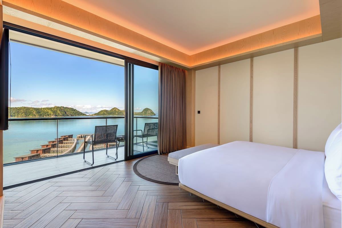 Ein Hotelzimmer mit einem großen Bett, Meerblick und einem Balkon mit Sitzgelegenheit.