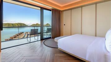 Habitación de hotel con una cama grande, vista al mar y balcón con mobiliario exterior.