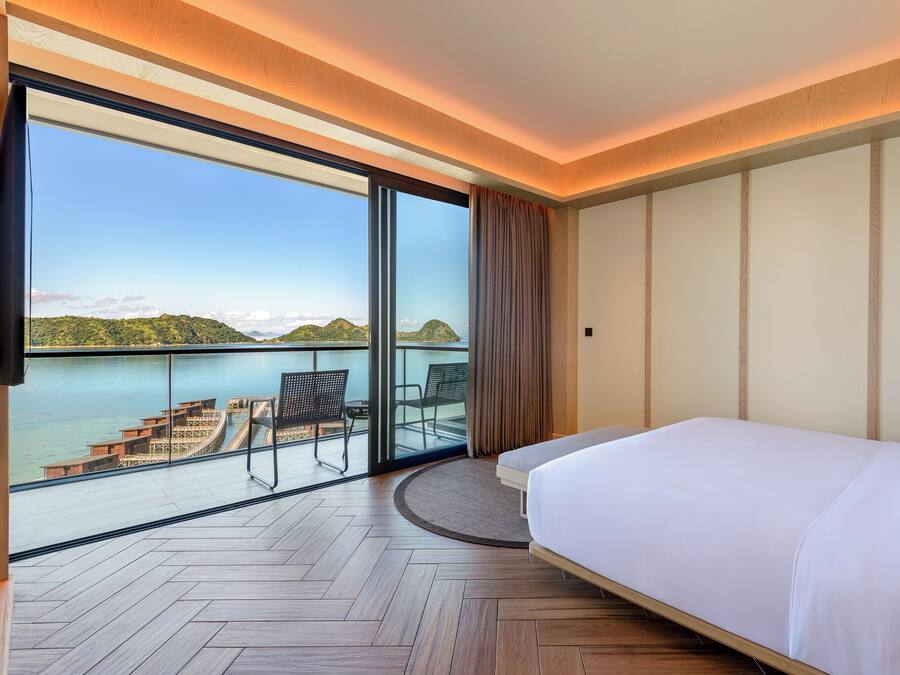 Habitación de hotel con una cama grande, vista al mar y balcón con mobiliario exterior.