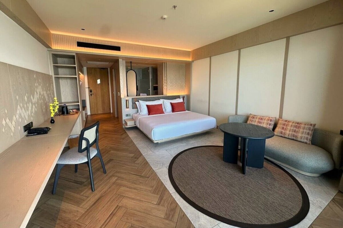 Ein modernes Hotelzimmer mit einem Bett, einem Schreibtisch, einem Sessel, einer Couch und einem runden Tisch.